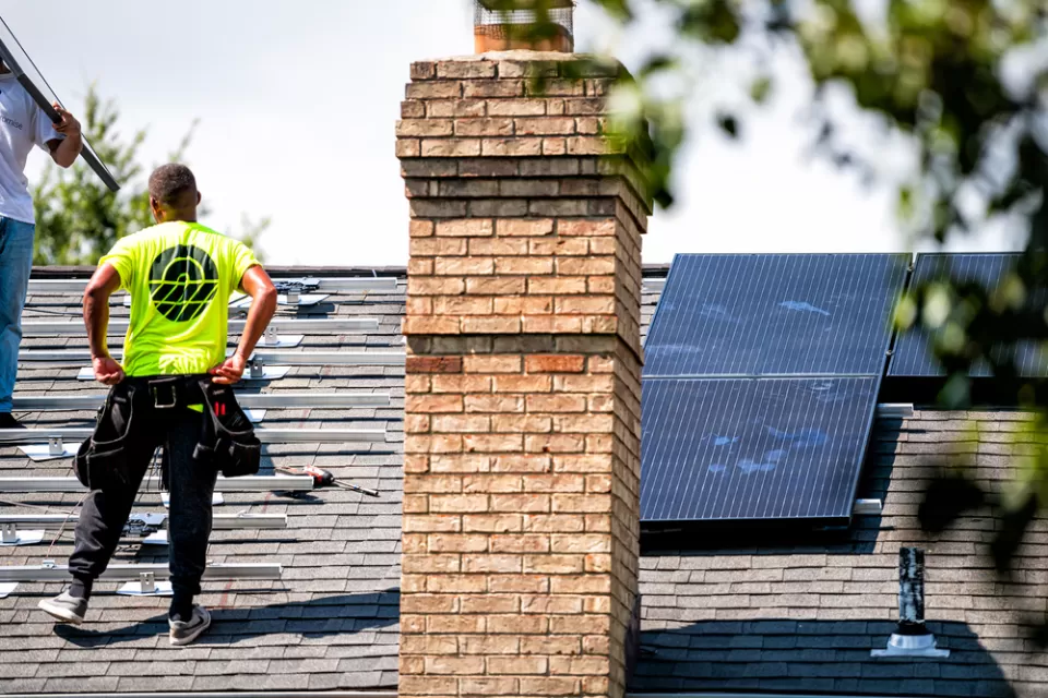 Roofers stand on top of a residential roof while installing solar panels.